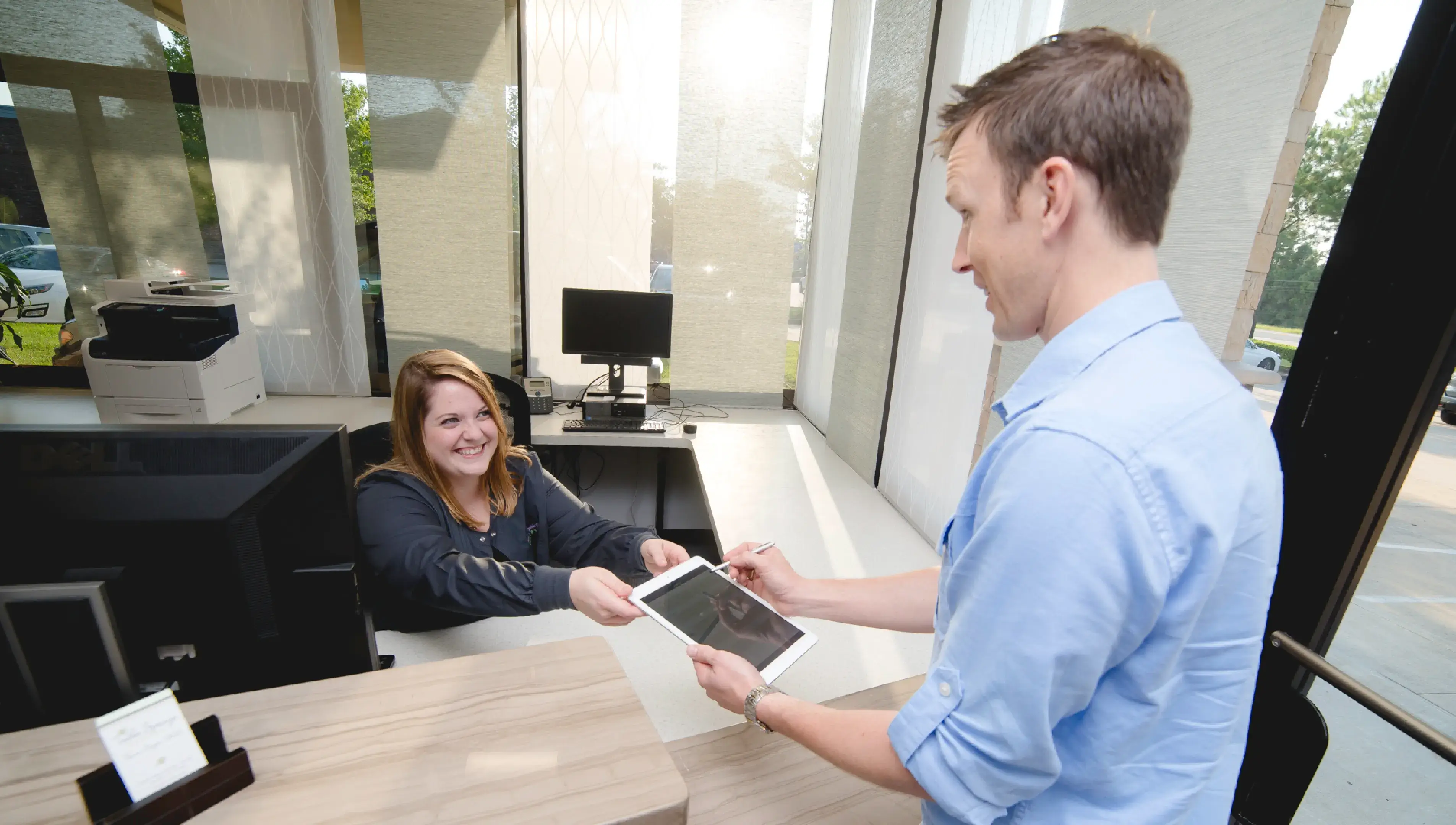 A man handing a woman a tablet computer.